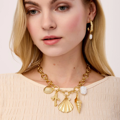 Woman wearing a gold necklace with shell charms on a light background