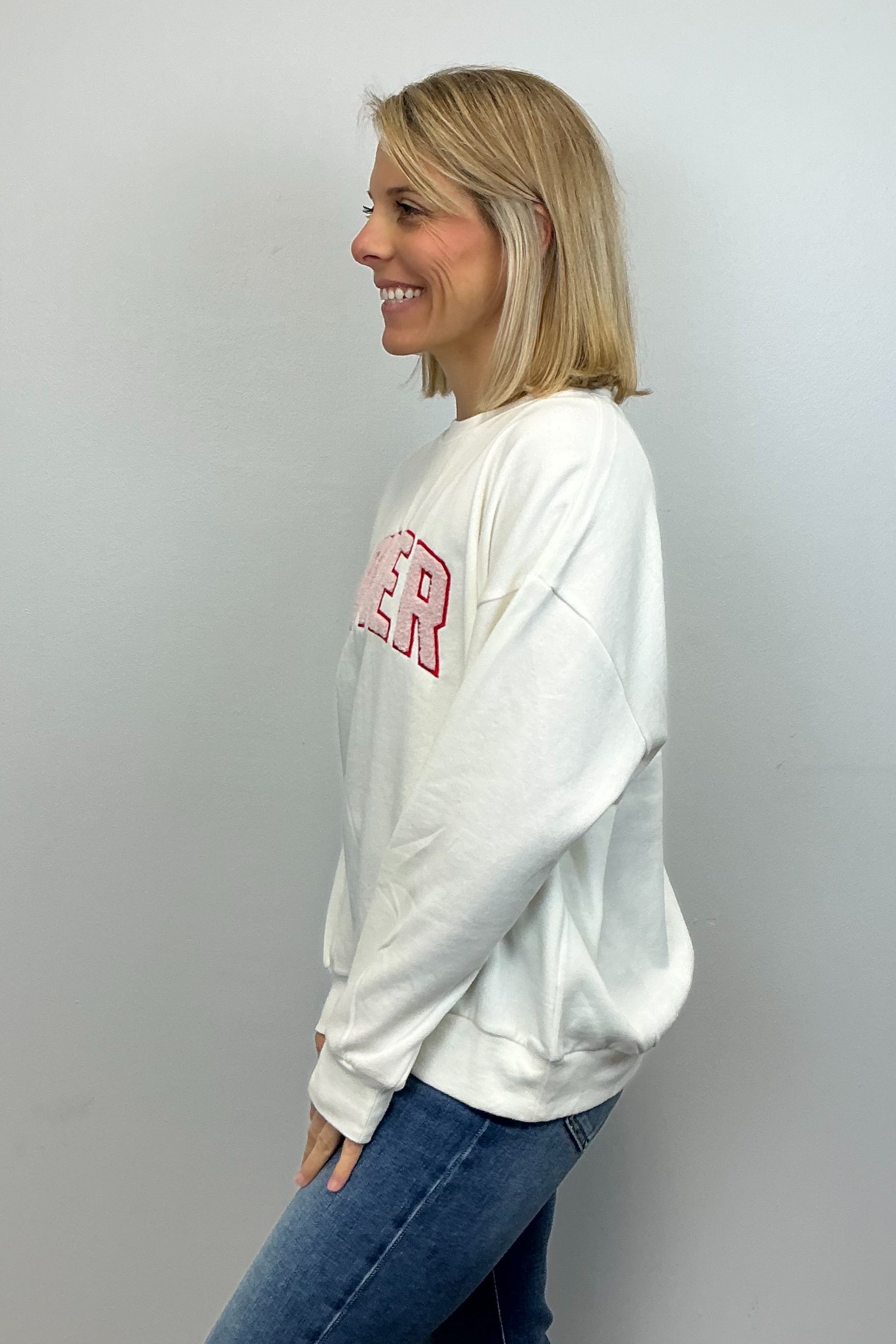 Woman wearing a white sweatshirt with red text and blue jeans against a plain background